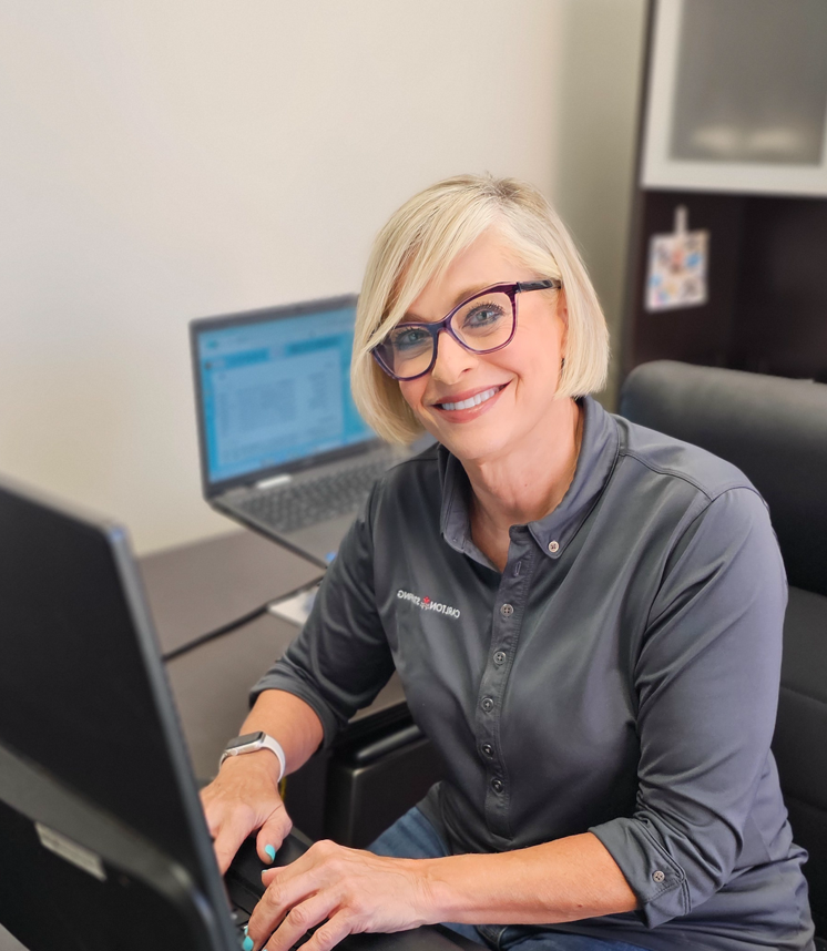 Professional blonde woman in glasses smiling at desk with laptop, typing.